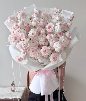 Bouquet of pink kiss of fairy rose spray with white ribbons on a neutral background.