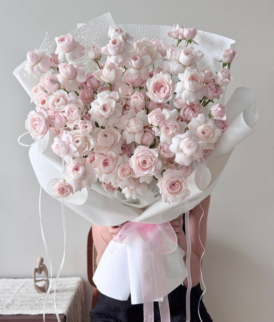 Bouquet of pink kiss of fairy rose spray with white ribbons on a neutral background.