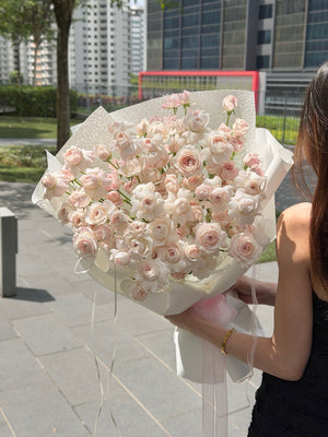 Person holding a large bouquet of pink kiss of fairy rose spray outdoors with buildings in the background