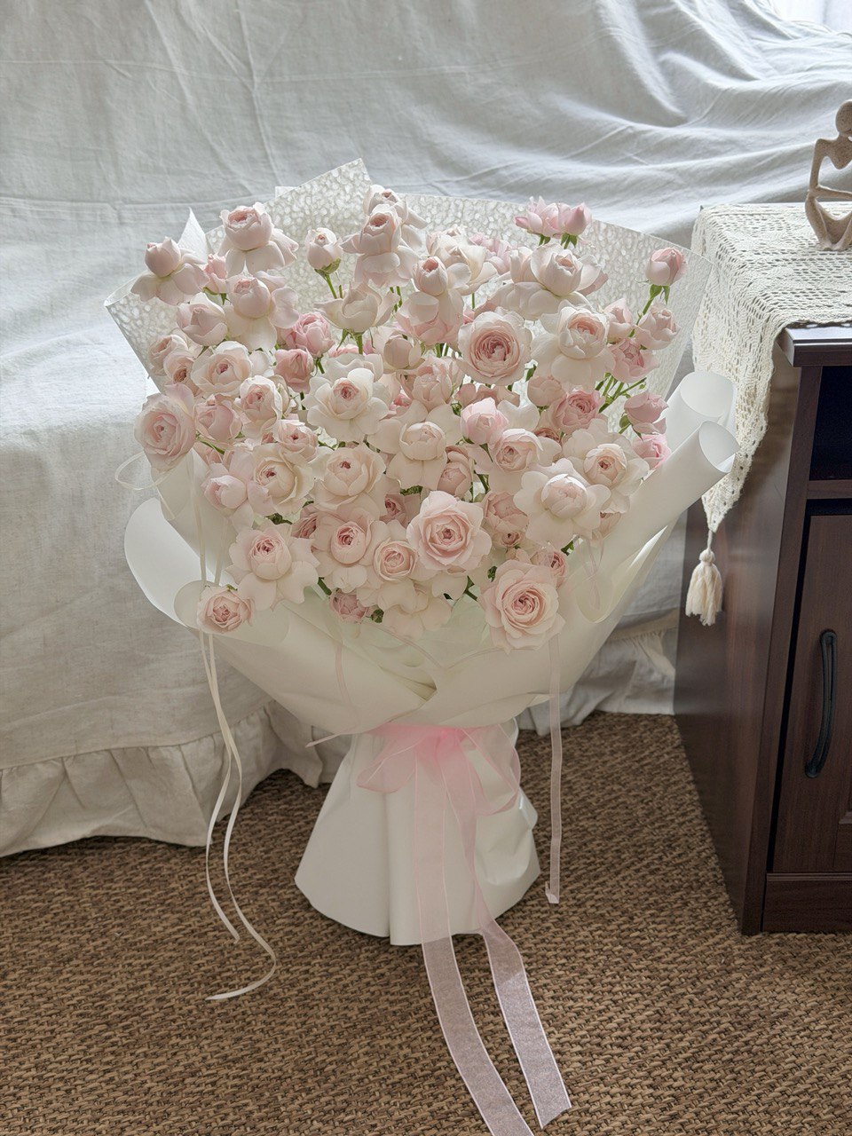 Bouquet of pink kiss of fairy rose spray flowers with a white ribbon on a carpeted floor.