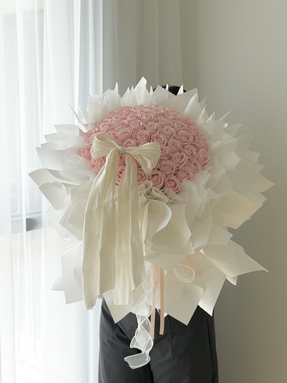 A large bouquet of pink roses wrapped in white wrapper with a cream satin bow, perfect for proposal flower gift.