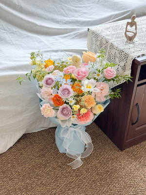 Bouquet of flowers in a light blue wrapper on a carpeted floor with a white curtain in the background.