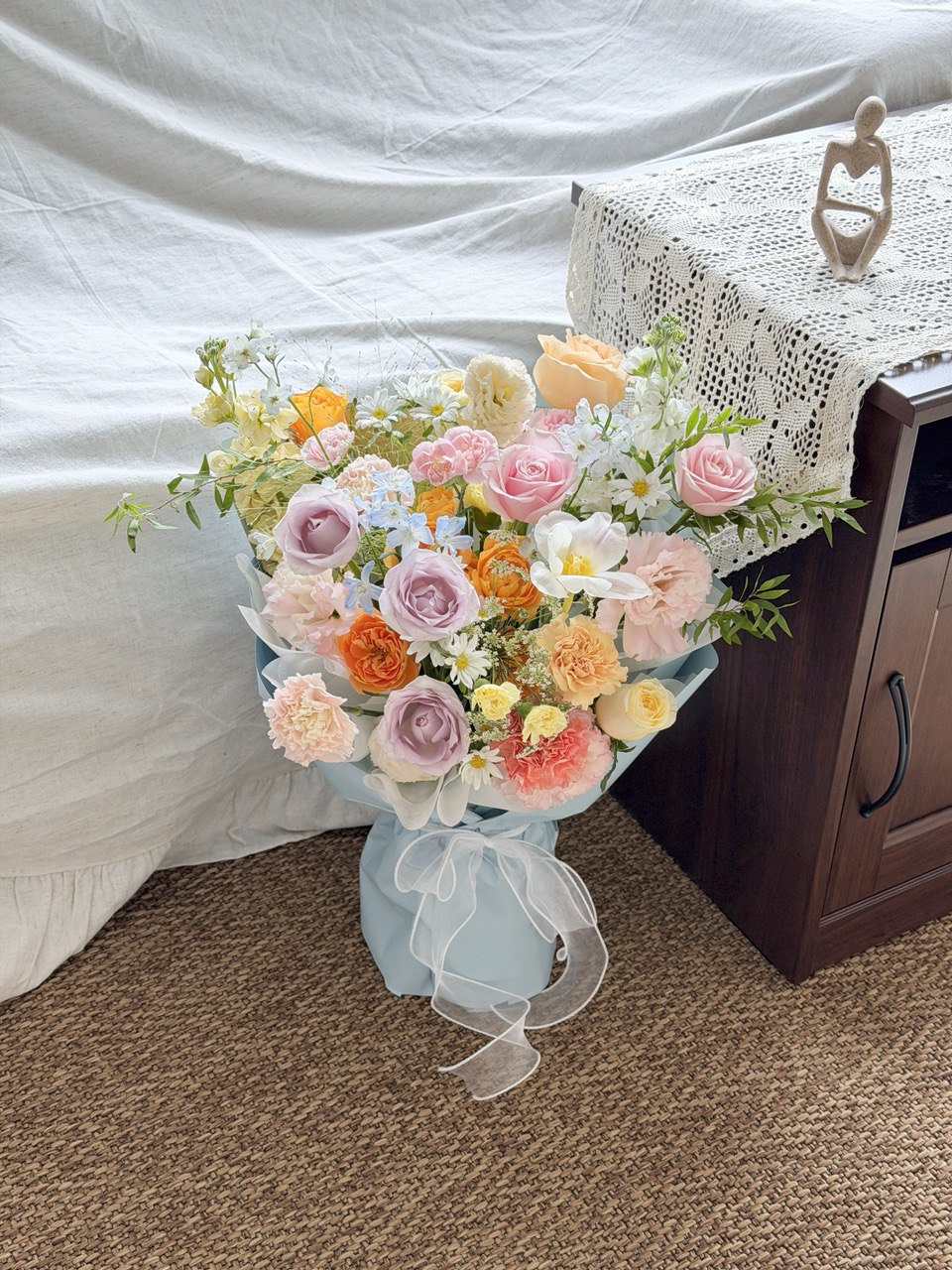 Bouquet of flowers in a light blue wrapper on a carpeted floor with a white curtain in the background.