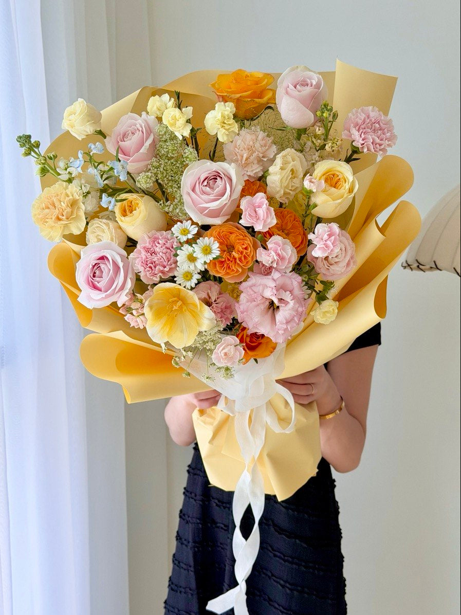 Cheerful pastel mixed rose bouquet with yellow wrapper featuring pink roses and orange flowers, perfect for birthday surprises and happy occasions.