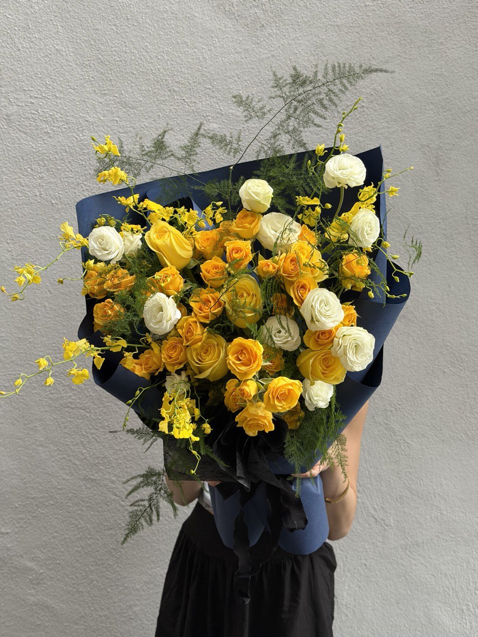 Bouquet of yellow, white, and orange roses with asparagus grass against a gray background at Kuala Lumpur.