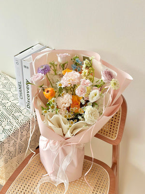Bouquet of flowers in a pink wrapper on a wicker chair with a book in the background