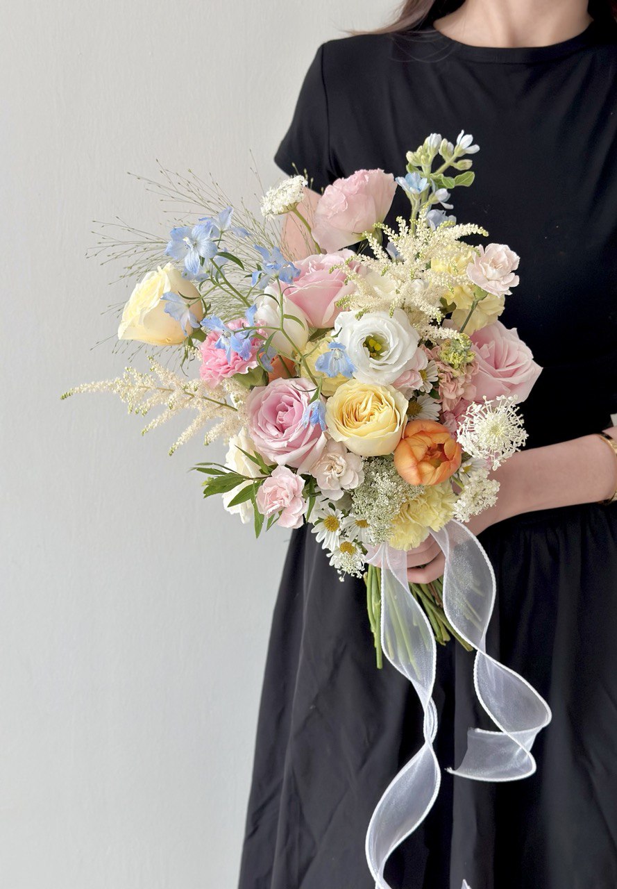 Bouquet of bridal pastel flowers held by a person wearing a black dress against a gray background