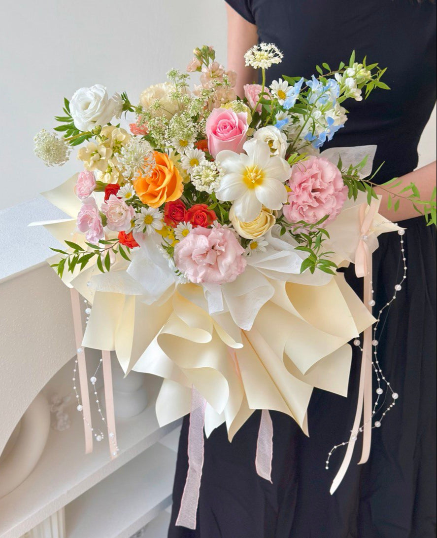 Close-up of a pastel floral arrangement with roses, carnations, and tulip, wrapped in layered cream wrapping paper.
