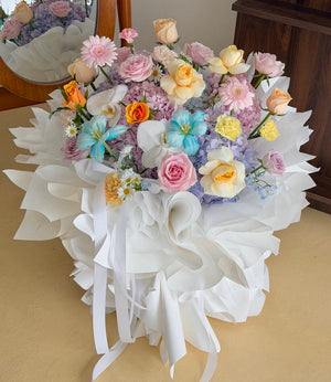A bouquet of Large hydrangea flower bouquet mixed with roses, gerbera, tulip and filler wrapped in ballet style white paper. 
