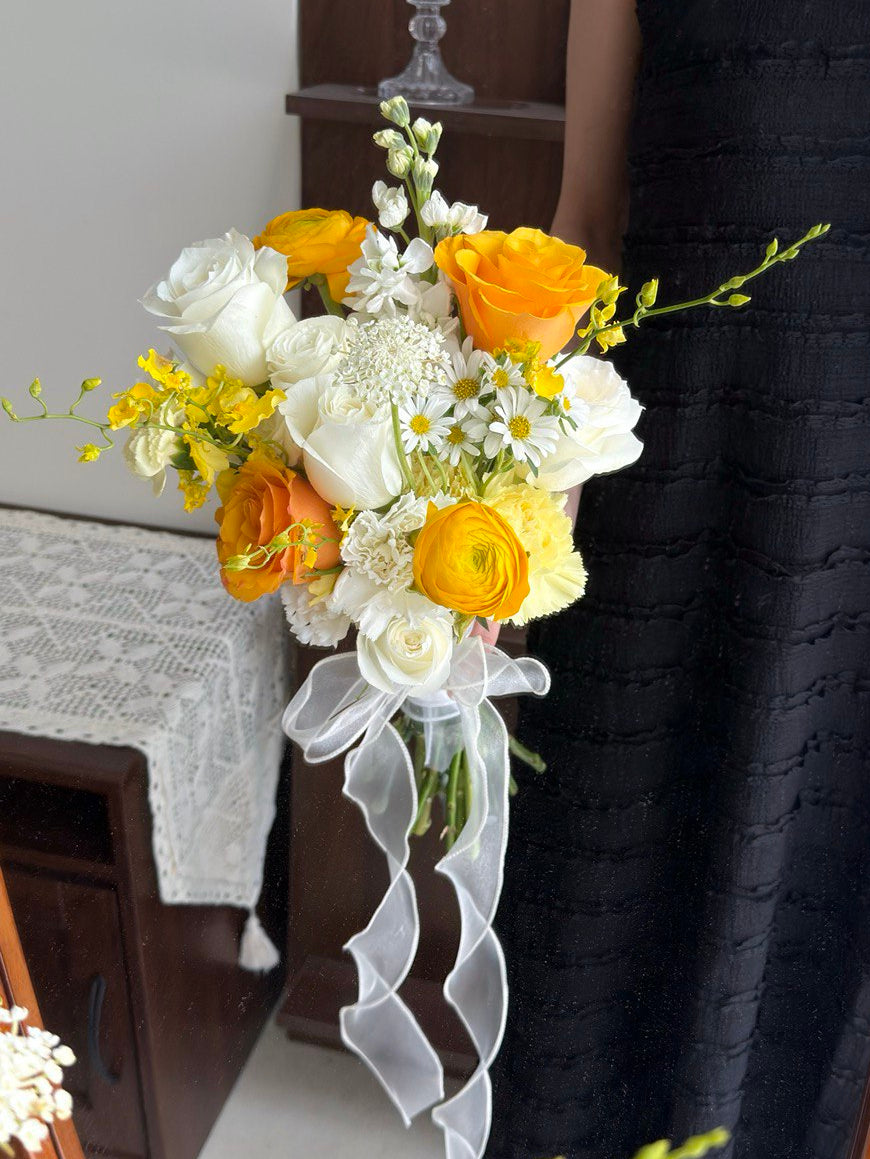 Bouquet of wedding flower with white and yellow flowers held by a person wearing a black dress in front of mirror.