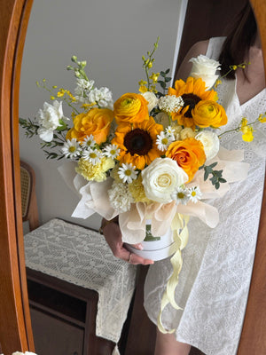 A girl is holding a box with sunflower, refulgence rose, dancing lady, white rose and hana white in front of a mirror.