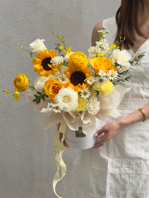 Bouquet of sunflower, refulgence rose, ranunculus and white rose in a box held by a person wearing a white dress at Kuala Lumpur.
