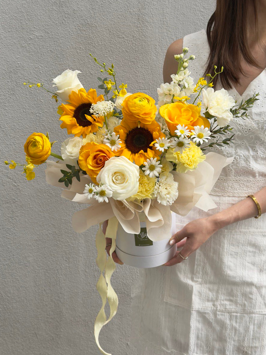 Bouquet of sunflower, refulgence rose, ranunculus and white rose in a box held by a person wearing a white dress at Kuala Lumpur.
