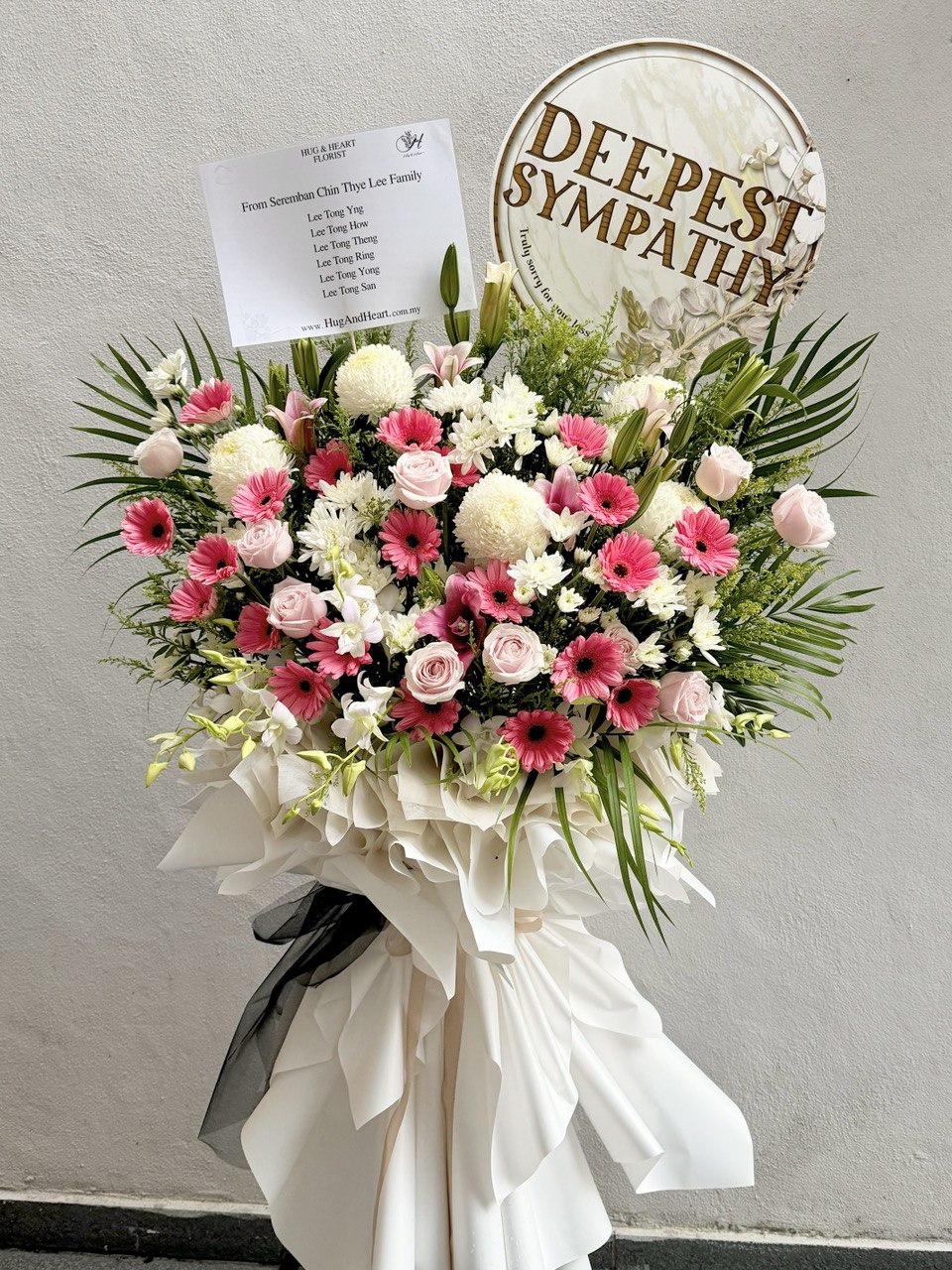 Floral arrangement with pink and white flowers, white ribbon, and 'Deepest Sympathy' sign on a gray background with delivery at Kuala Lumpur and Selangor.