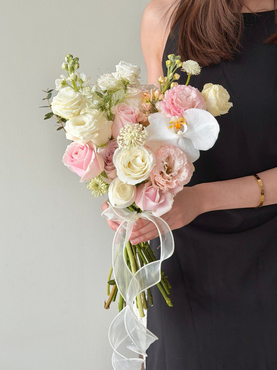 A girl wearing black dress is holding a bouquet of wedding ROM flower consists of pink roses, white roses, white phalaenopsis and some Eustoma with same day delivery at Kuala Lumpur and Selangor.