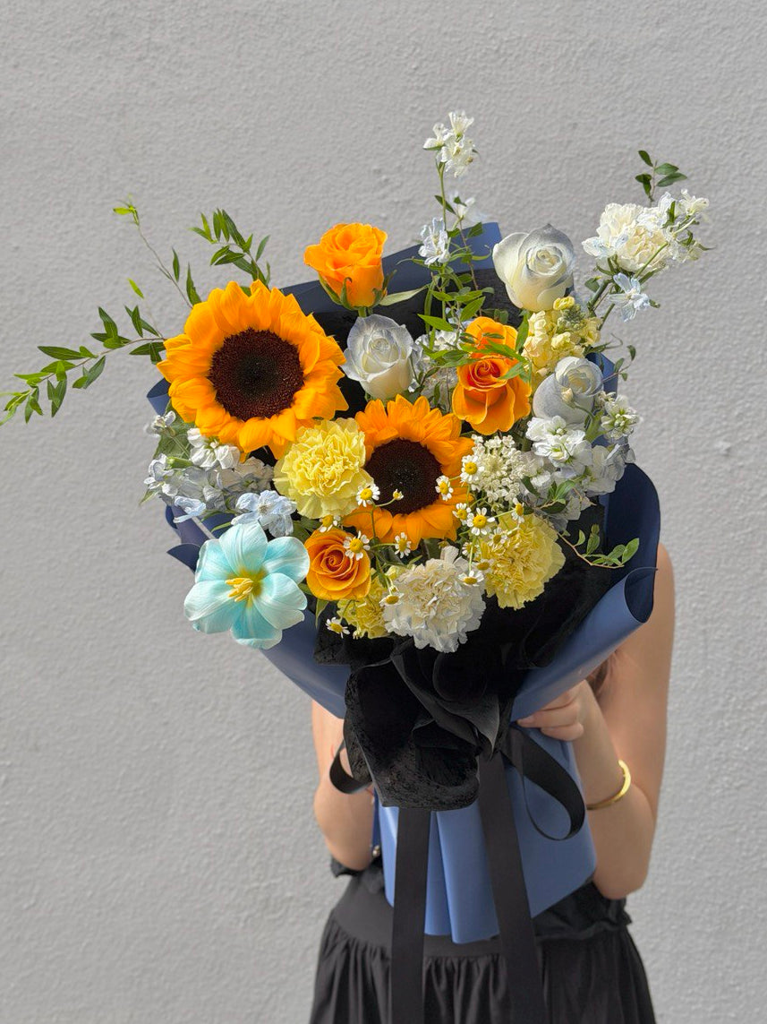 Bouquet of sunflowers with dye tulips, refulgence rose, white rose, white matthiola, yellow carnation and chamomile  held by a person against a gray background for graduation.