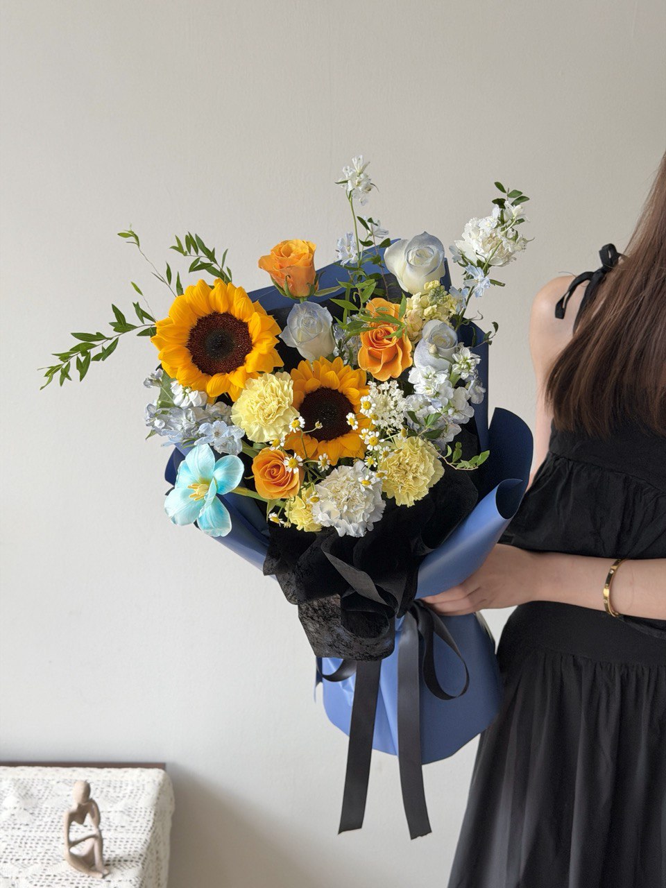 Sunflower and pastel rose graduation bouquet held by a woman in a black dress.
