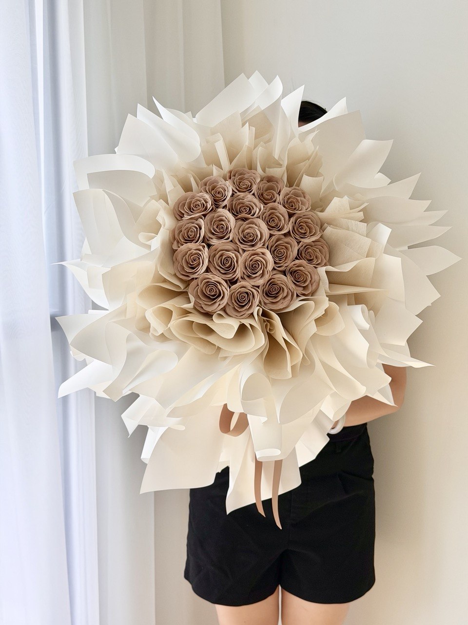 A girl wearing black is holding a bouquet of cappuccino rose soap flower wrapped in white ballet wrapper - perfect flower delivery for proposal event.