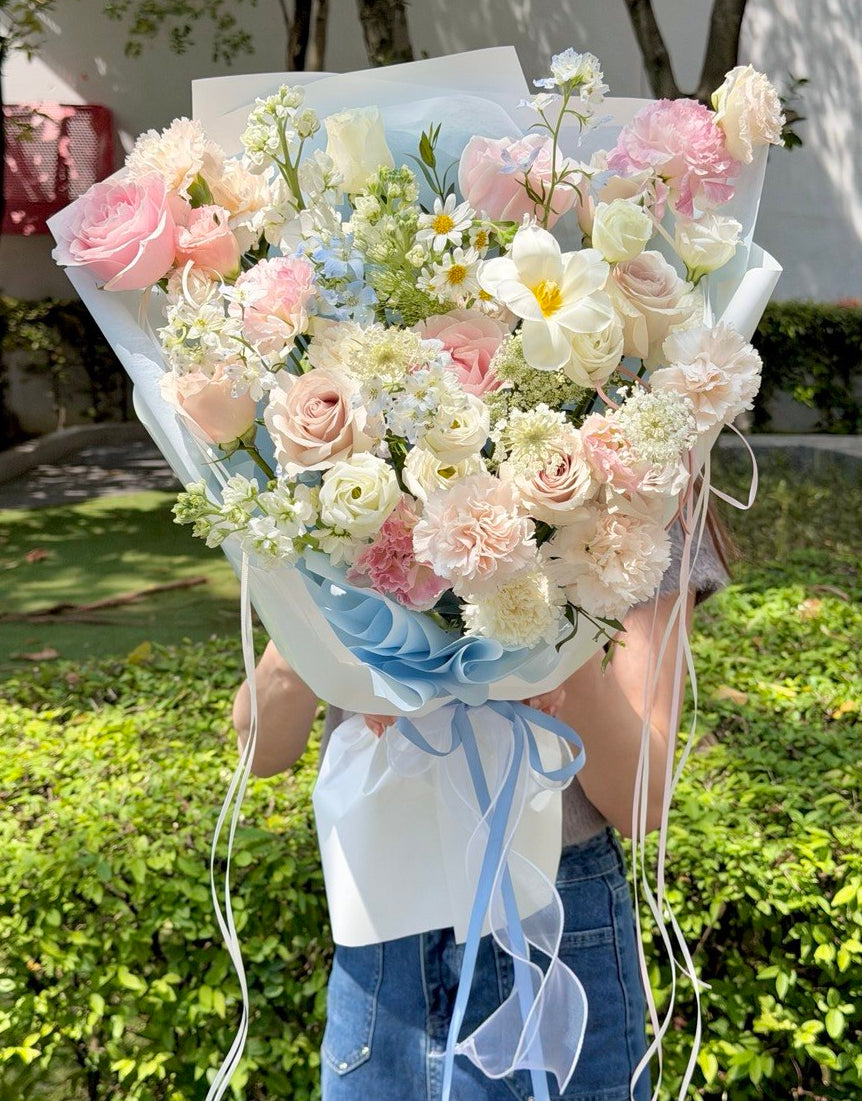 Large blue and pink flower bouquet featuring premium pink roses, blue delphinium, white narcissus, carnations, and seasonal mixed fillers, held by a girl with same-day flower delivery in Kuala Lumpur and Selangor.