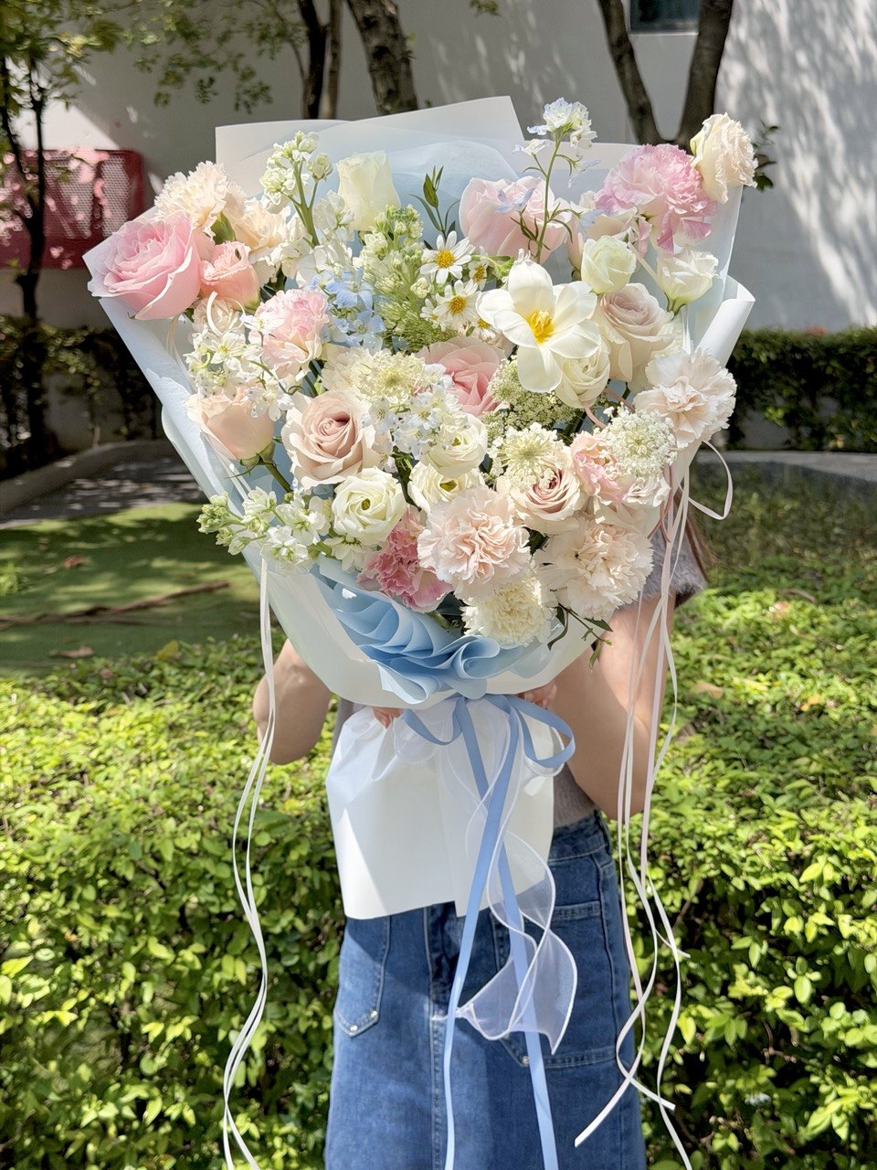 Large blue and pink flower bouquet featuring premium pink roses, blue delphinium, white narcissus, carnations, and seasonal mixed fillers, held by a girl with same-day flower delivery in Kuala Lumpur and Selangor.