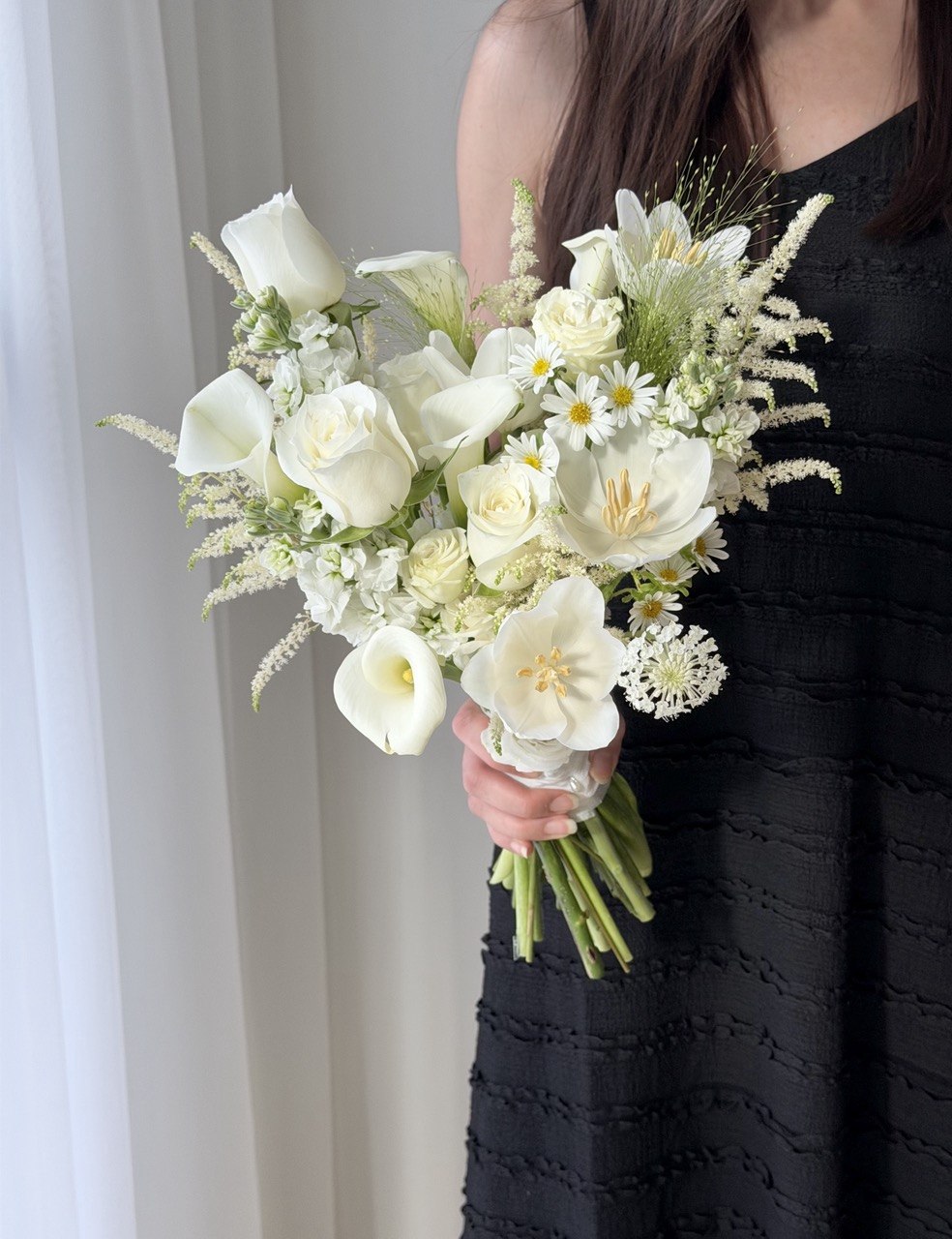 A girl wearing a black dress in holding a bridal hand bouquet featuring calla lily and estilbe.