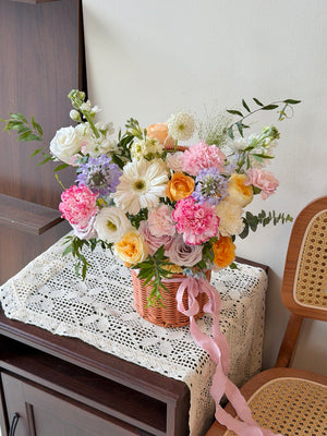 Bouquet of flowers in a basket on a lace tablecloth with a chair in the background.