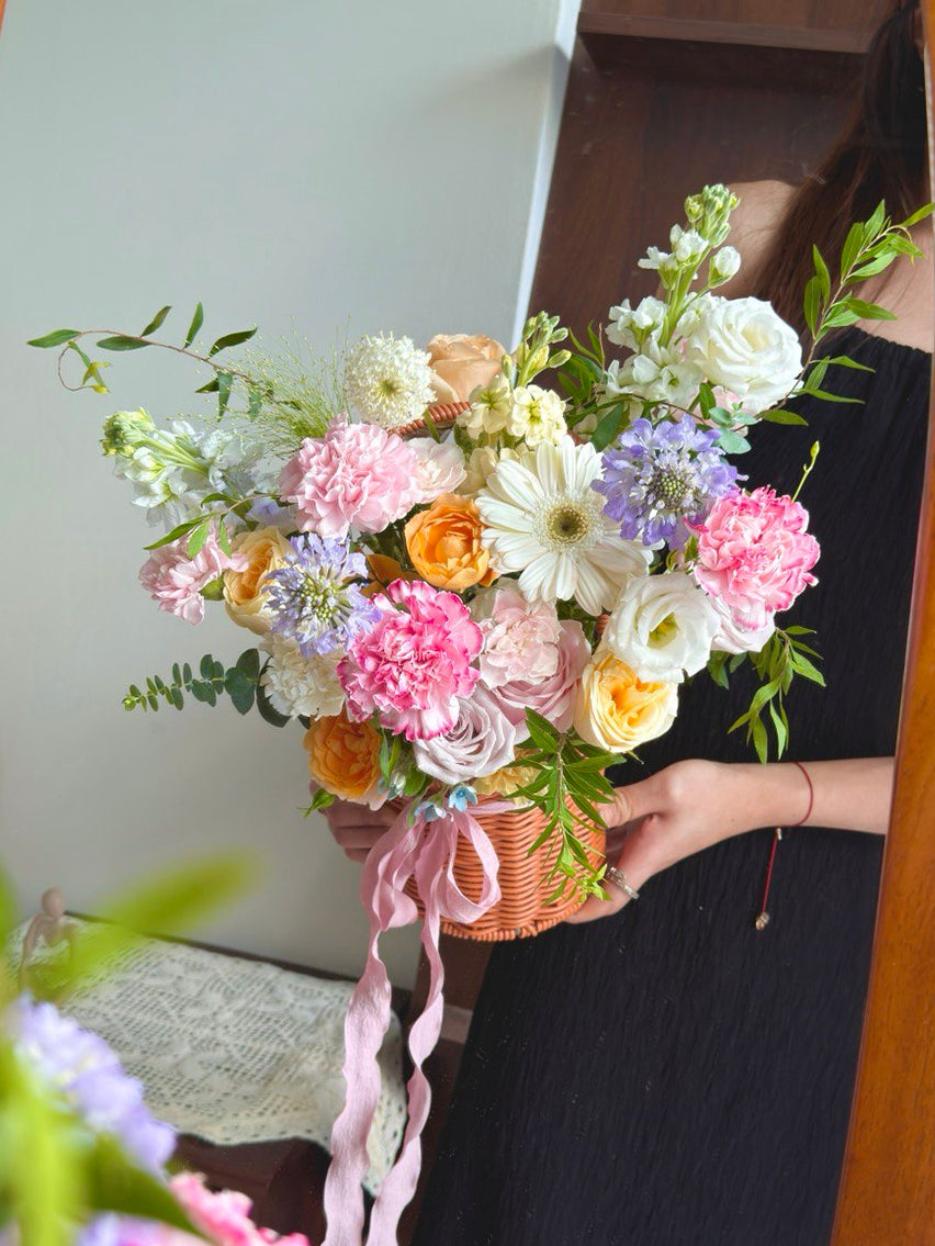 Person holding a basket of colorful flowers in front of a mirror.