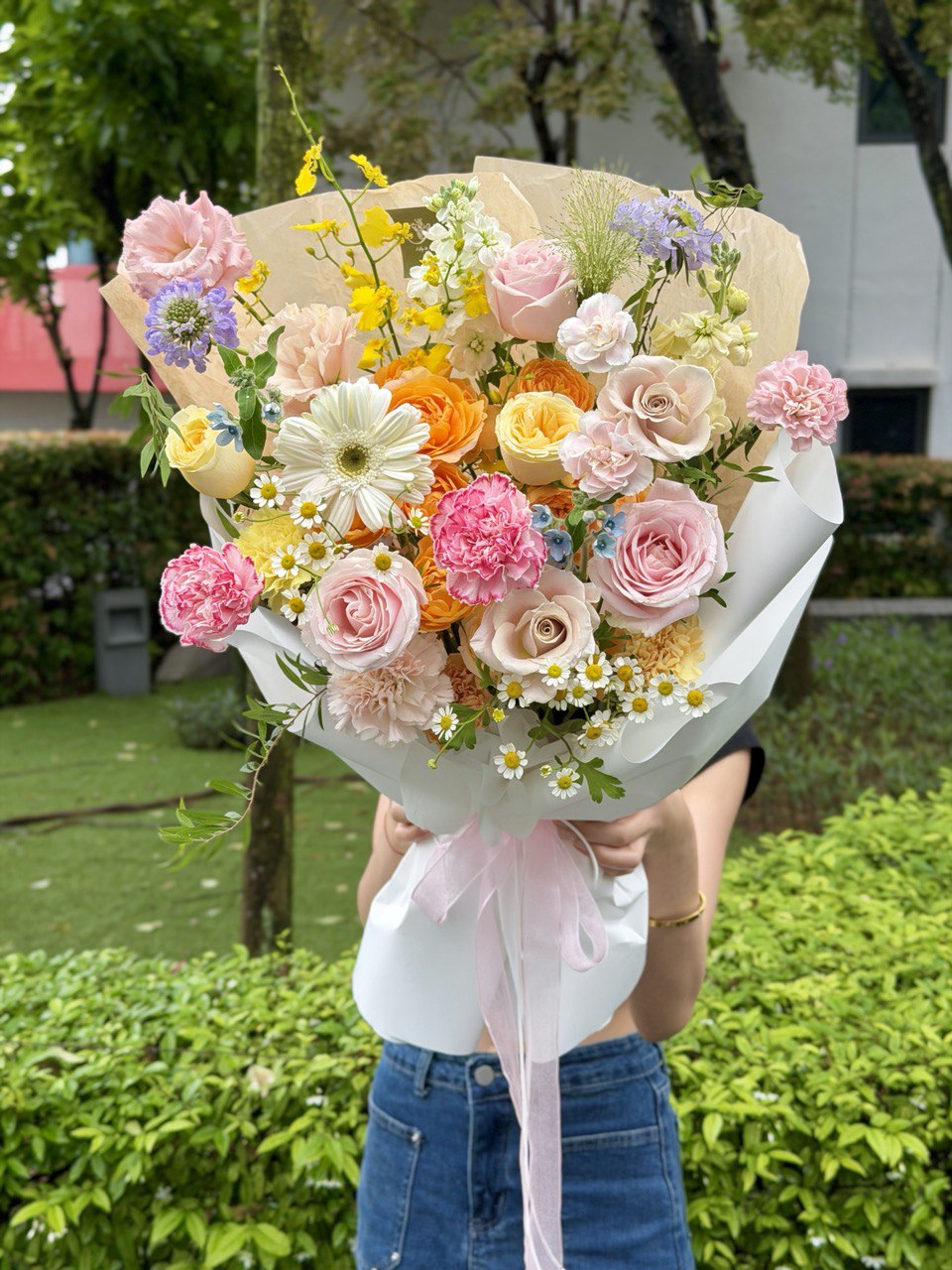 Fresh pastel flower arrangement with pink roses, chamomile daisies and seasonal blooms wrapped in white wrapping.