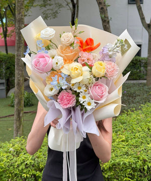 A women wearing black dress is holding a vibrant flower bouquet featuring orange tulip, buttercup rose. Bouquet shop near me at Subang Jaya.