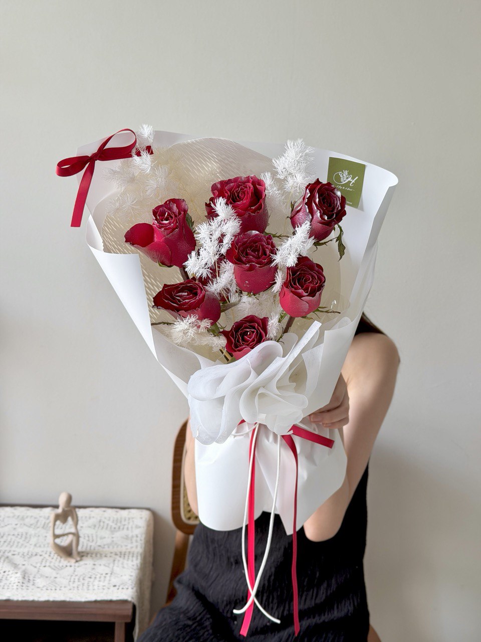 Bouquet of red roses with white accents design for Christmas gift held by a person against a neutral background.