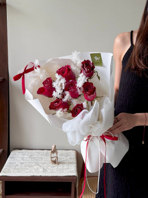 Person holding a bouquet of red roses and white flowers wrapped in white paper with a red ribbon perfect for this Christmas flower gift.