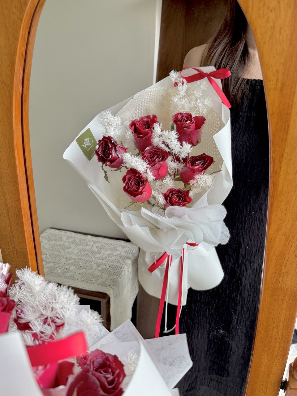 Bouquet of red roses with white accents in a decorative paper wrap, held by a person in front of a mirror.