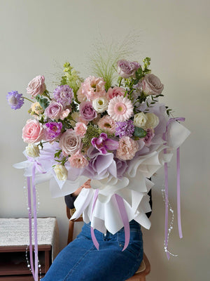 Romantic pastel flower arrangement with lilac roses, blush and cream flowers wrapped in premium white wrapping, ideal for special occasions.