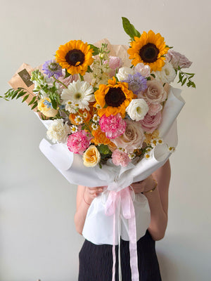 Bouquet of flowers with sunflowers and roses held by a person against a plain background.