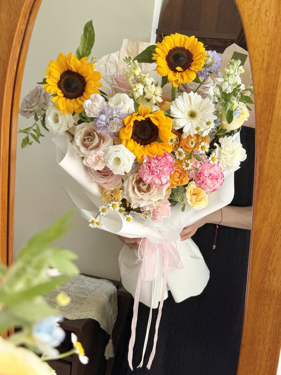 A girl is standing infront of a mirror holding her graduation sunflower bouquet.