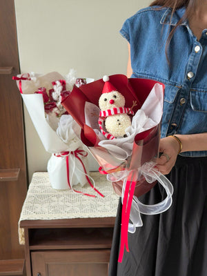 Person holding a bouquet with a snowman decoration, standing next to a table with wrapped gifts.