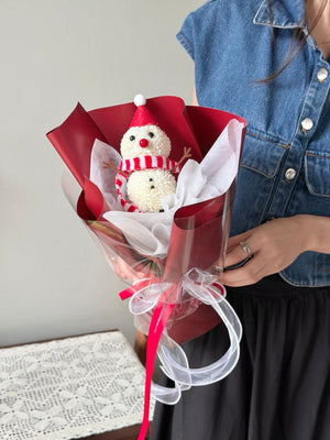 Bouquet with a snowman decoration held by a person wearing a denim jacket.