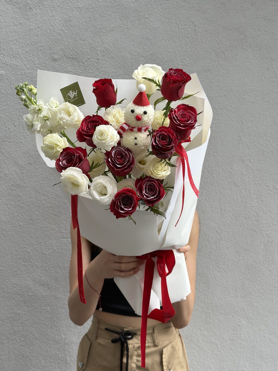 Bouquet of red and white flowers with a snowman decoration against a gray background.