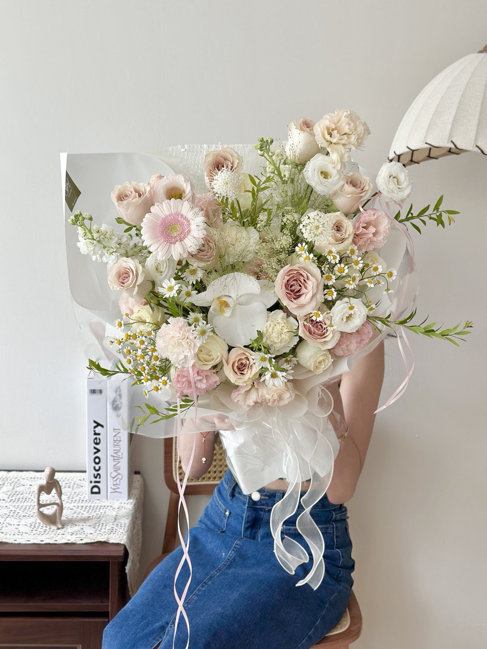 Bouquet of quicksand rose mixed with fillers flowers held by a person wearing blue jeans in a room setting.