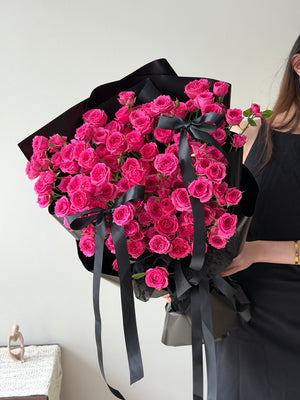 A girl is holding a large bouquet of hot pink rose spray wrapped in black paper and ribbons.