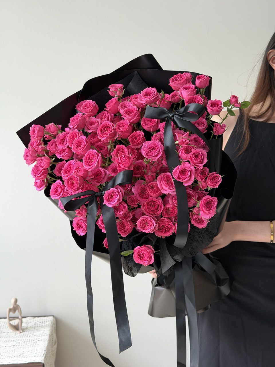 A girl is holding a large bouquet of hot pink rose spray wrapped in black paper and ribbons.