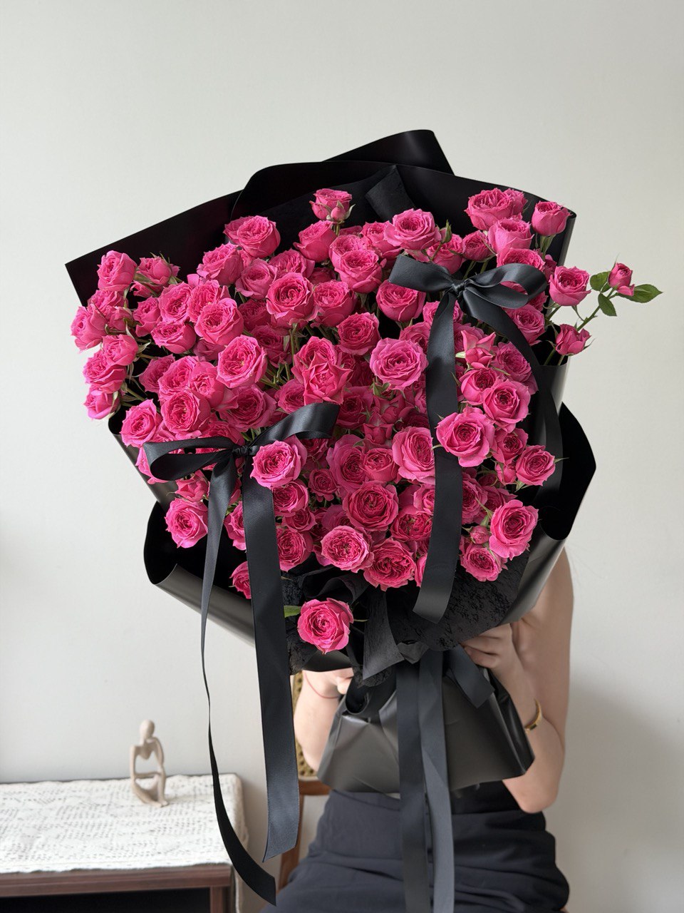 Bouquet of hot pink rose spray wrapped in black paper with a black ribbon on a white background.