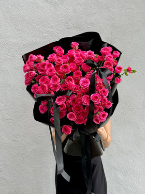Bouquet of hot pink roses wrapped in black paper held by a person against a gray background perfect for birthday and anniversary gift.