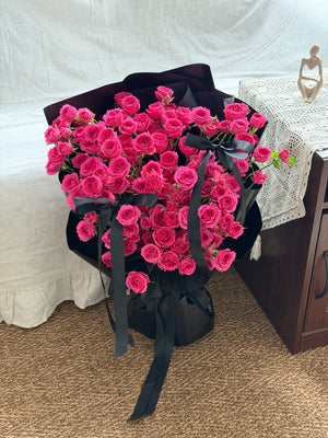 Bouquet of hot pink rose spray wrapped in black paper with ribbons on a carpeted floor at Kuala Lumpur.