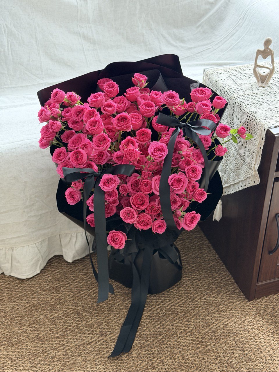 Bouquet of hot pink rose spray wrapped in black paper with ribbons on a carpeted floor at Kuala Lumpur.