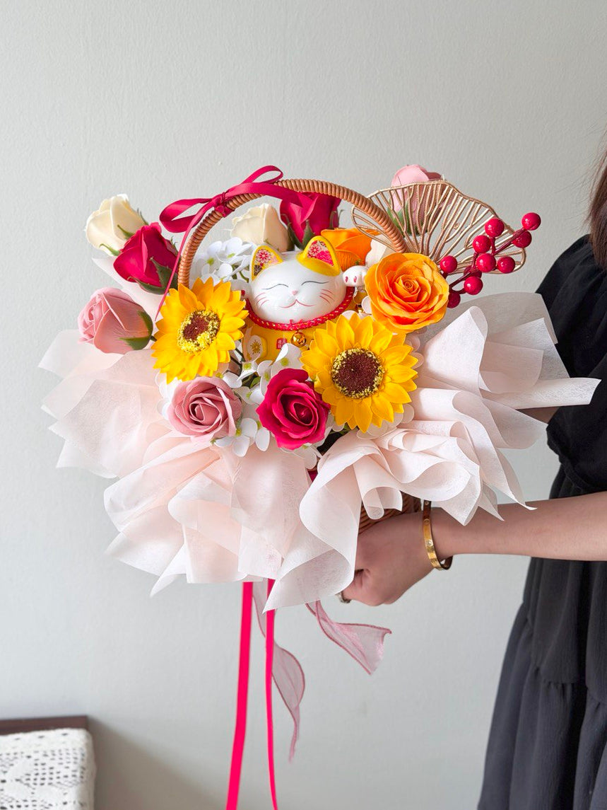 A basket with soap flowers and a small cat figurine held by a person against a plain background.