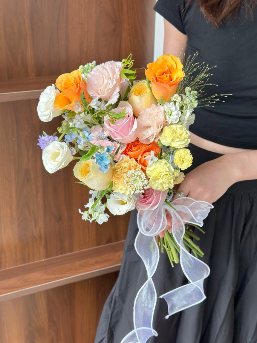 Colorful bridal bouquet featuring vibrant refulgence roses, buttercup rose, and soft pastel flowers, tied with a sheer ribbon.