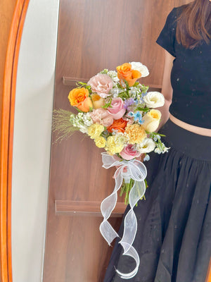 Bright wedding hand bouquet with yellow, orange, and pastel pink roses, accented with carnations and delicate fillers, Malaysia florist design.