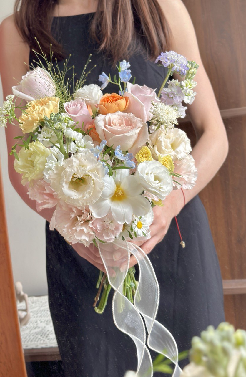 Elegant wedding bouquet with pastel roses, cream carnations, and light blue fillers tied with organza ribbon.