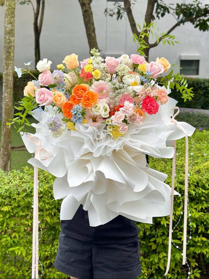 Bouquet of flowers with white paper wrap held by a person outdoors.